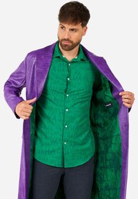 Purple faux leather long coat with a textured finish, worn over a green shirt featuring a repeating "HA" pattern. Interior lined with a graphic print.