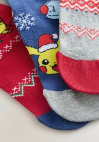 Kolme värikästä jouluteemalla varustettua sukkaa; yksi, jossa on Pikachu jouluhatussa, ja kaksi, joissa on punaisia, valkoisia ja vihreitä juhlavia kuvioita.