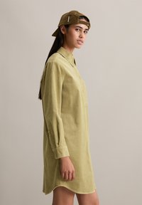 Katoenen shirtjurk in lichtgroen, met een kraag, lange mouwen en een ontspannen pasvorm. Gecombineerd met een bruine pet. Glad textuur.