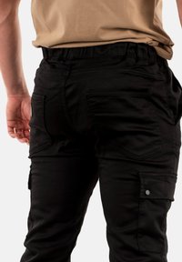 Zwarte cargo broek met elastische tailleband, meerdere zakken en een gladde, duurzame stofstructuur. De achterkant benadrukt de details van de zakken.