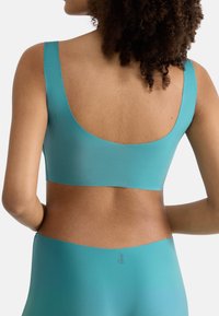 Teal sportsbh med brede stropper, glat tekstur og scoop-bagdesign, parret med matchende højttaljede underdele med et logo.