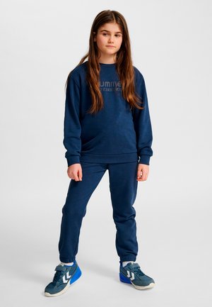 Marinblå bomulls-sweatshirt med texturerad logotyp, matchad med joggers i samma färg. Modellen bär grå och blå sportskor med framträdande designdetaljer.