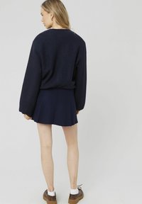 Pull marine avec des manches bouffantes, associé à une jupe plissée marine. Modèle portant des chaussures brunes avec des chaussettes blanches. Design simple, texture douce.