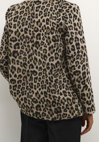 Giacca con stampa leopardata in beige e nero, caratterizzata da una texture morbida, vestibilità comoda e colletto a punte. Il retro mostra un motivo di grandi macchie.