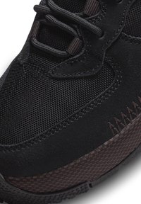 Mustat urheilukengät, joissa on teksturoitua verkkoa ja mokkajäljitelmää, tummanruskeita yksityiskohtia, kova pohja ja hienostuneet tikkaukset.