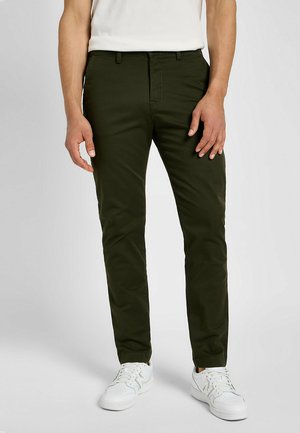 Dunkelgrüne Chinos aus Baumwolle, slim-fit Design mit geradem Bein, ausgestattet mit Fronttaschen und getragen mit weißen Sneakern.