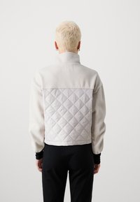 Tikkitakki, jossa on kodikas pinta, vaaleanharmaa fleeceyläosa ja timanttikuvioitu materiaali takaa alhaalla.