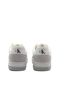 Sneaker bianche con tomaia in pelle liscia, dettagli in suede grigio sul tallone e logo "CK" nero. Suola in gomma testurizzata con nome del marchio.