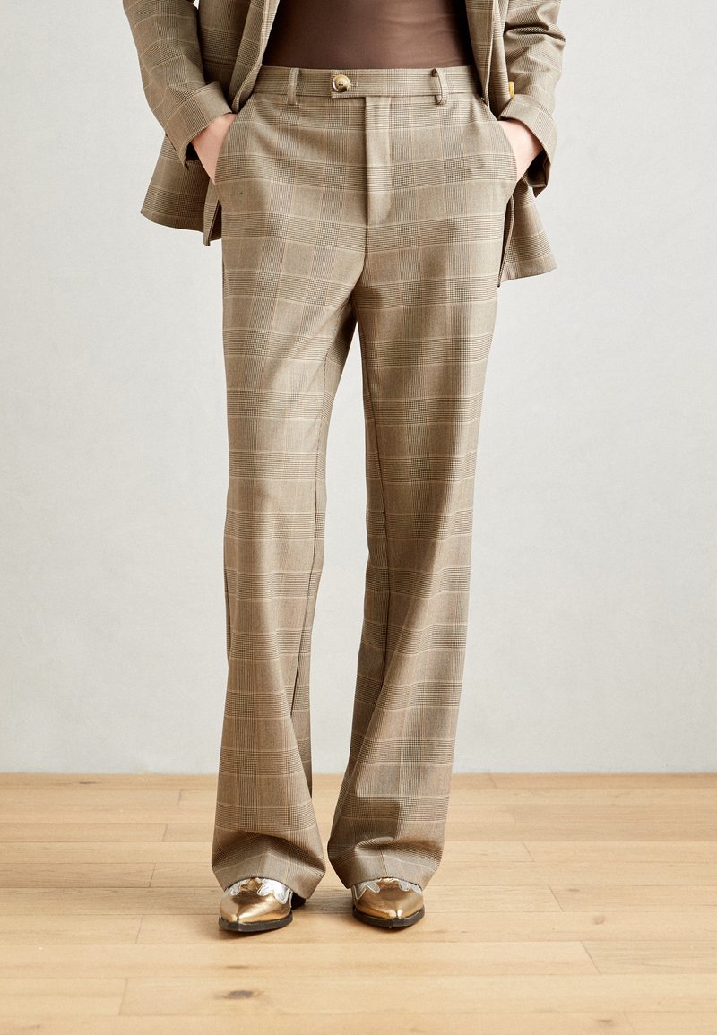 Un pantalon à carreaux beige avec une coupe ajustée, comportant des poches avant et une fermeture à bouton. Le tissu présente un tissage texturé, mettant en valeur le design.