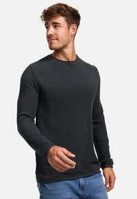 Cămașă lungă, gri închis, cu guler rotund și material texturat, purtată cu blugi bleu deschis, evidențiind un design ajustat.