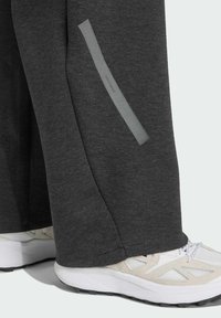 Tmavošedé tepláky so bočnými reflexnými prúžkami a mäkkou textúrou, spolu s svetlými športovými topánkami so sieťovinovým detailom.