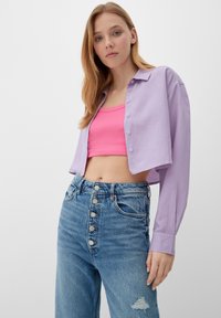 Lila cropped shirt met lange mouwen en knoopsluiting, gedragen over een roze geribbelde tanktop en hoge, versleten denim jeans.