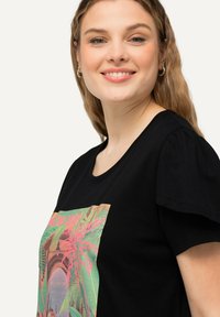 T-shirt nera a maniche corte con una vivace grafica di palme in rosa e verde. Tessuto di cotone morbido con una vestibilità rilassata e scollo rotondo.