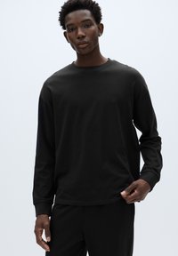 Černé tričko s dlouhým rukávem z měkké látky s kulatým výstřihem. Má volný střih a žebrované manžety. Jednoduchá a jednotná textura.