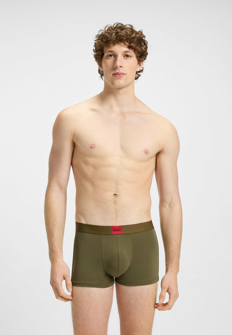 Boxer da uomo verdi con una cintura logo rossa; realizzati in tessuto morbido, presentano una vestibilità attillata e una lunghezza fino a metà coscia.