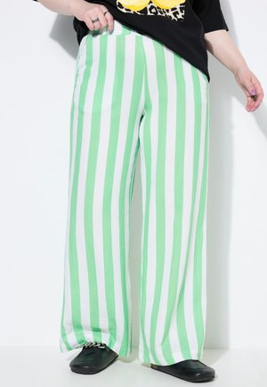 Pantalones de pierna ancha a rayas verdes y blancas, confeccionados en una tela suave, con un ajuste relajado y una textura sutil. Unos zapatos negros complementan el conjunto.
