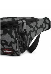 Svart och grå camo midjeväska med en texturerad yta, två fack med dragkedja, justerbar rem och märkespatch.