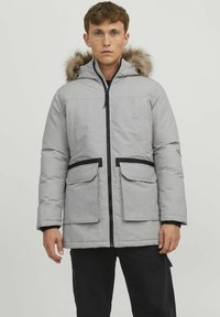 Pilkas paminkštintas parka tipo kailinis su kailio apvadu ant gobtuvo, užtrauktuko uždarymas, dvi priekinės kišenės, juodos akcentai ir elastinės rankogaliai. Minkšta tekstūra.