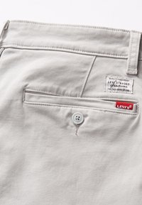 Pantalones gris claro con cierre de botón y un bolsillo trasero que presenta una etiqueta de Levi's. Tela suave y detalles de costura neat.
