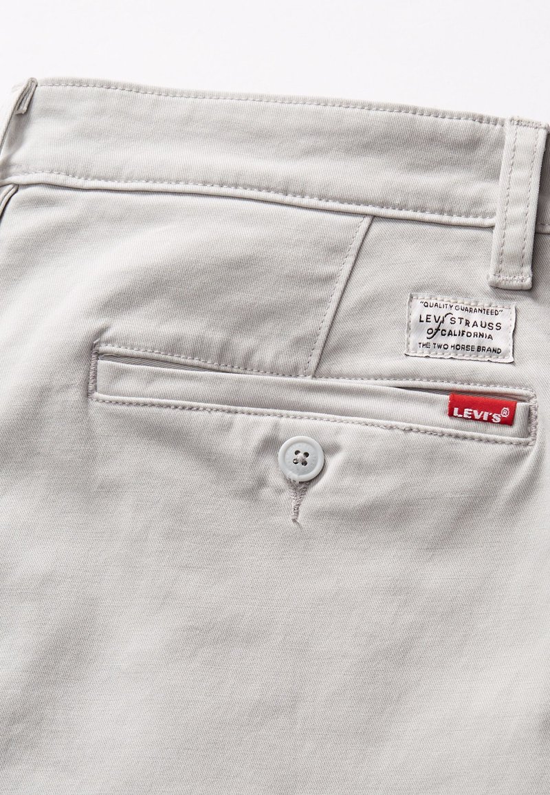 Pantalones gris claro con cierre de botón y un bolsillo trasero que presenta una etiqueta de Levi's. Tela suave y detalles de costura neat.