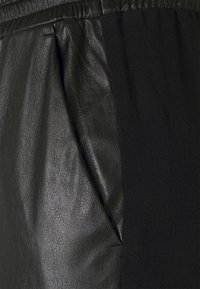 Pantalon noir avec un panneau en cuir texturé et un côté en tissu doux, doté d'une taille élastique et d'un détail de poche latérale.