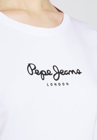 T-shirt en coton blanc avec un logo en script noir "Pepe Jeans" en dessous, "LONDRES", col rond, texture lisse et sans motifs.
