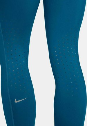 Nike leggings in teal met een gladde textuur hebben ventilatiegaten en een klein zilveren logo nabij de enkel. Strak ontwerp.