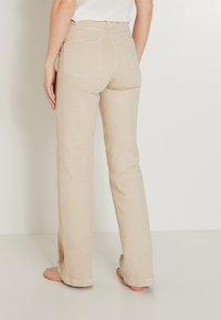 Jeans beige de cintura alta con un diseño de pierna recta, que presentan bolsillos traseros y costuras visibles, mostrados desde una vista trasera.