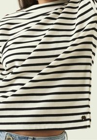 Vit och svart randig kortärmad topp med en fyrkantig silhuett, tillverkad av mjukt tyg. Har en liten hjärtformad logotyp vid fållen.