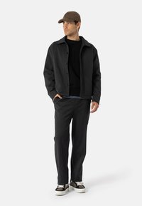 Ciemnoszary wełniany płaszcz z zapięciem na guziki, nałożony na czarny sweter, w zestawieniu z dopasowanymi spodniami i brązową czapką w kratę. Całość dopełniają casualowe sneakersy.