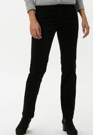 Pantalones de pana negra con un diseño de pierna recta, que cuentan con bolsillos delanteros y una superficie texturizada. Combinados con botas de tacón negro hasta el tobillo.