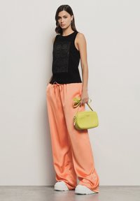 Top nero senza maniche con design testurizzato, pantaloni alla zuava beige chiaro con cordoncino, scarpe bianche e una piccola borsa gialla.