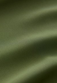 Strukturierter grüner Stoff mit einem subtilen gerippten Muster, das eine glatte, weiche Oberfläche und einen leichten Glanz zeigt; geeignet für verschiedene textiltechnische Anwendungen.
