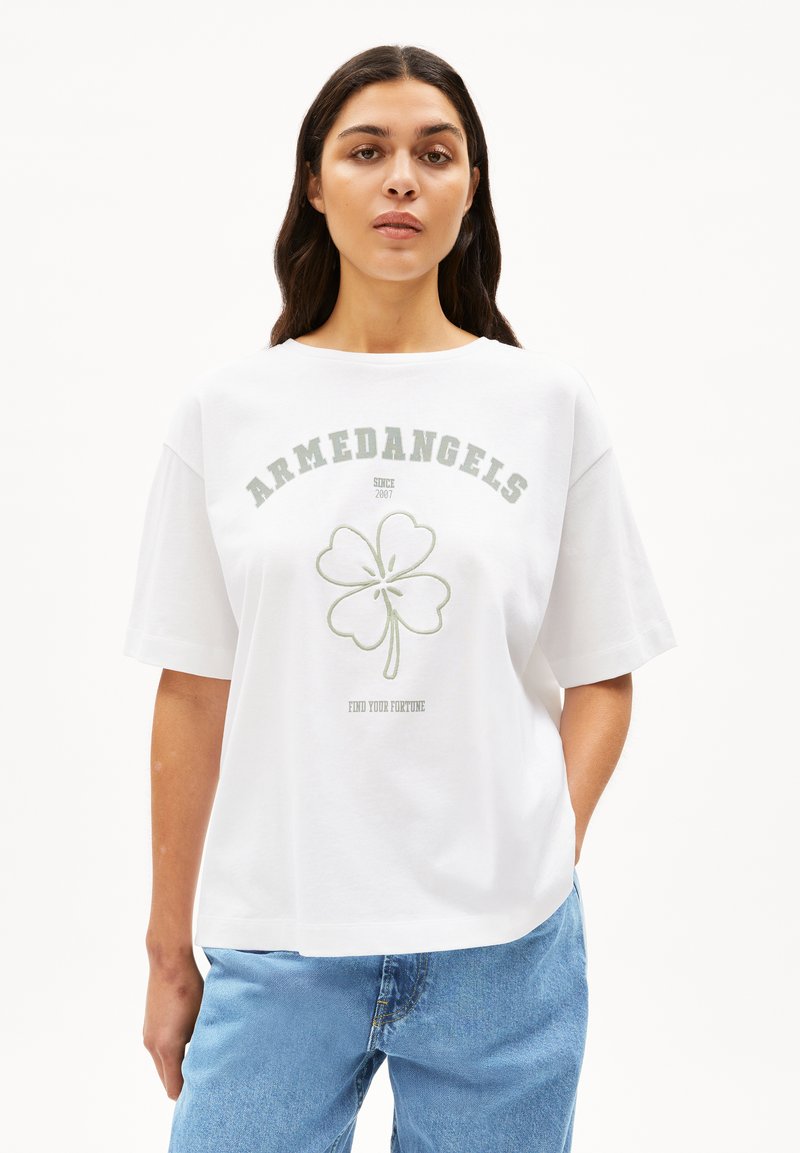 Witte katoenen t-shirt met korte mouwen en een ronde hals, met een groene vierbladige klavertopdruk en de woorden "ARMEDANGELS" en "VIND JOUW FORTUIN."