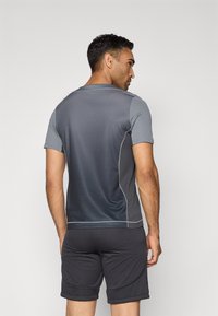 Grå idretts T-skjorte med korte ermer, med en gradient design. Kombinert med svarte shorts; begge har en glatt tekstur og tettsittende fasong.