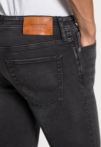 Svarta denimjeans med en läderetikett med "JACK & JONES" på baksidan, fem fickor och subtila sömnadsdetaljer.