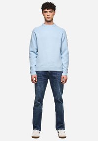 Helles blaues Sweatshirt aus Strickstoff, mit Rundhalsausschnitt und gerippten Bündchen, kombiniert mit dunklen Jeans und weißen Sneakern.