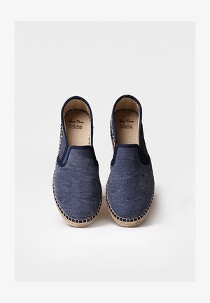 Zapatillas de lona azul marino de tipo slip-on con suela de yute cosida, puntera redonda y sin cordones. El interior cuenta con una etiqueta de marca impresa.