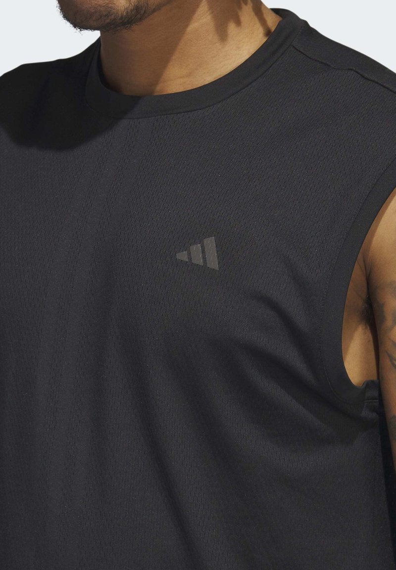 Camiseta atlética sin mangas de color negro, hecha de una tela texturada. Presenta un pequeño logo discreto en el pecho. El diseño incluye un escote redondo y agujeros para los brazos en forma de corte.