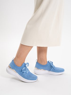 Lower legs wearing light blue knit sneakers with white soles and rhinestones, paired with cream-colored cropped pants.