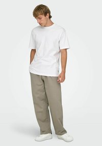 Biała bawełniana koszulka z krótkim rękawem, w połączeniu z jasnoszarymi spodniami o luźnym kroju i białymi trampkami. Prosty design, bez widocznych wzorów.