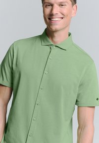 Korte mouw polo shirt in lichtgroen, gemaakt van zachte stof met een gladde textuur, heeft een kraag en zes knopen aan de voorkant.