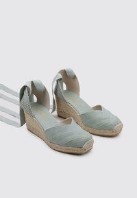 Wedges de esparto en verde menta con tiras cruzadas y suelas de yute tejidas. Textura de ante con un acabado suave y una plantilla ligeramente acolchada.