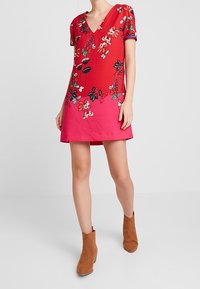 Rotes Blumenkleid mit V-Ausschnitt, kurzen Ärmeln und Ombre-Design, das zu Rosa verblasst. Verfügt über bunte Blumenmuster auf dem Stoff.