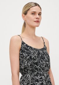 Vestido negro floral con tirantes finos, que presenta una cintura fruncida y sutiles patrones de flores blancas en una tela texturizada. Elegante y ligero.