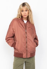 Chaqueta bomber en color rosa, hecha de un suave tejido de nailon. Presenta puños y dobladillo de canalé, cierre de cremallera y bolsillos laterales.