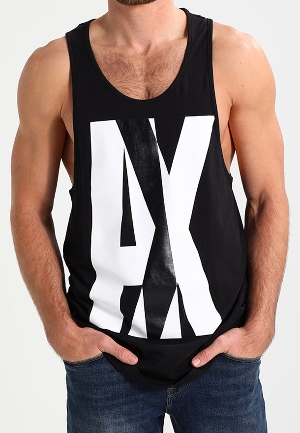Homme portant un débardeur noir avec de grandes lettres blanches et noires superposées « AX », les mains dans les poches, assorti à un jean bleu.