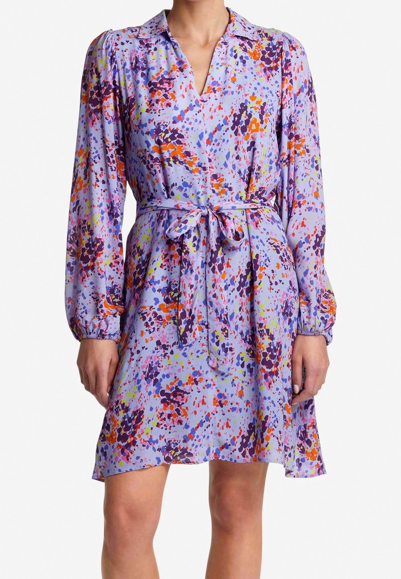 Fioletowa sukienka z żywym nadrukiem w plamy w kolorach czerwonym, pomarańczowym, zielonym i niebieskim. Posiada kołnierz, długie rękawy oraz związany w pasie. Gładka tekstura.