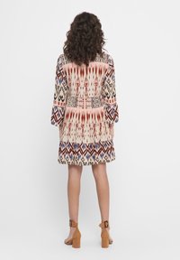 Vestido de manga acampanada con un patrón tribal multicolor con acentos en beige, rojo y azul. Tejido suave, con dobladillo de volantes en capas.