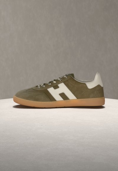 Pantof sport din piele întoarsă verde măsliniu, cu călcâi din piele albă și un mare "H" alb pe lateral, talpă din cauciuc maro și șireturi cu model, pe o suprafață gri.